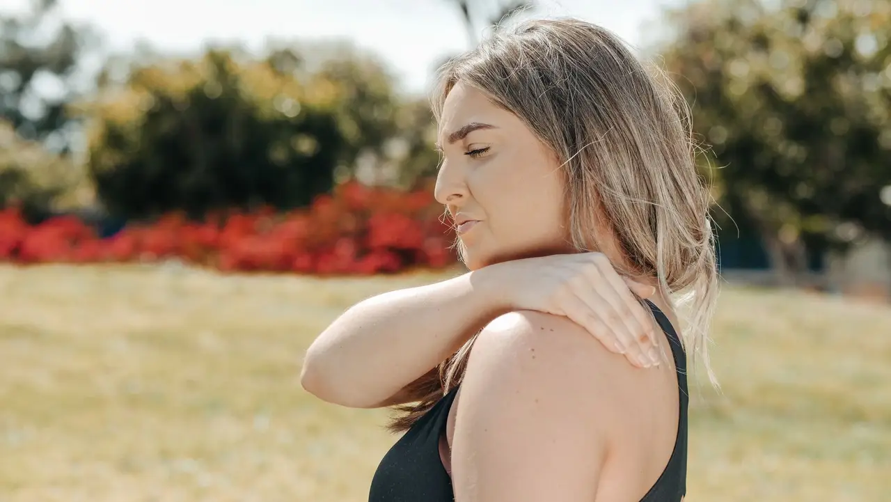 Mulher de regata preta ao ar livre com a mão apoiada sobre o ombro