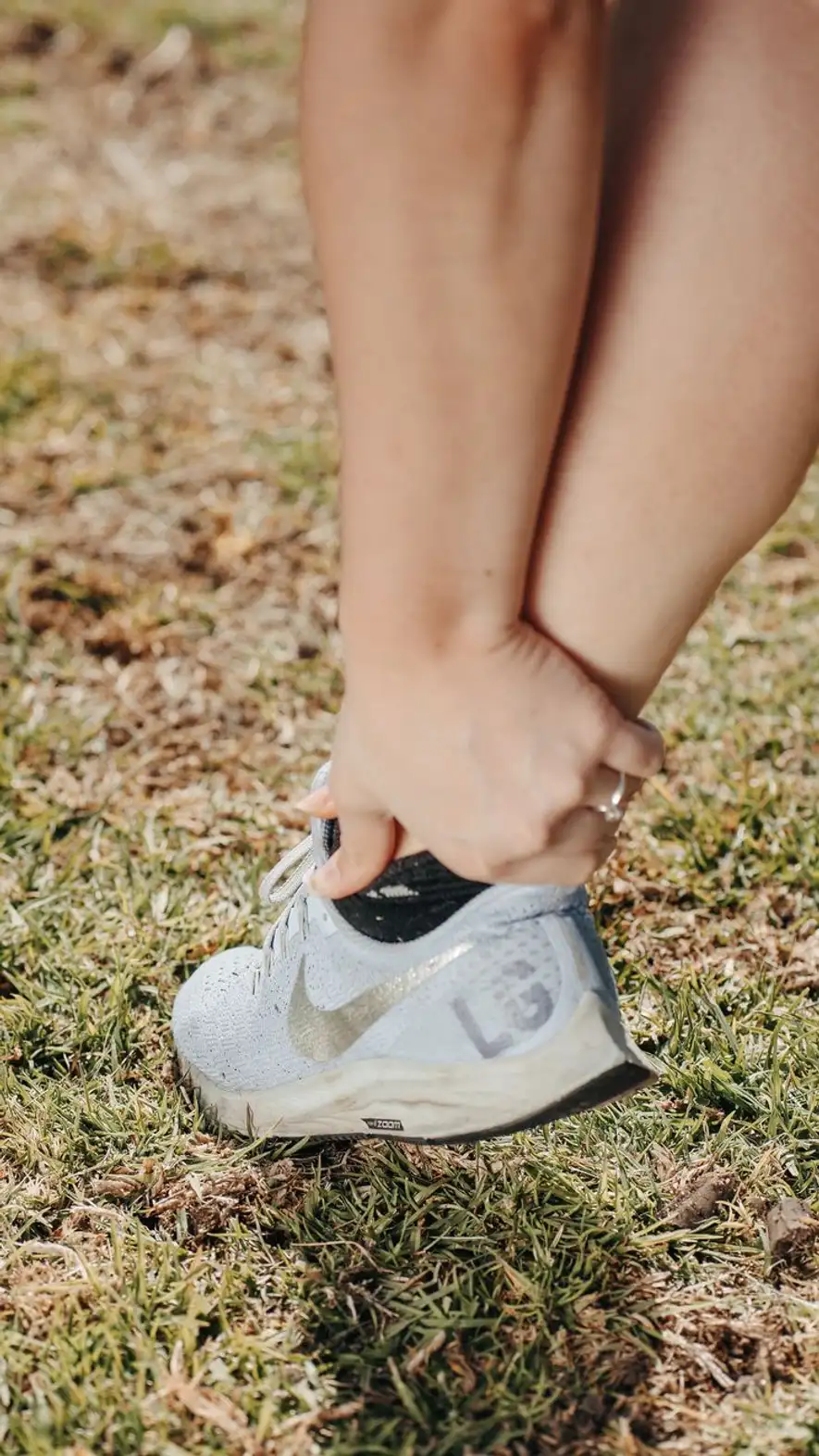 Mão segurando o tornozelo acima de um tênis de corrida, sobre a grama