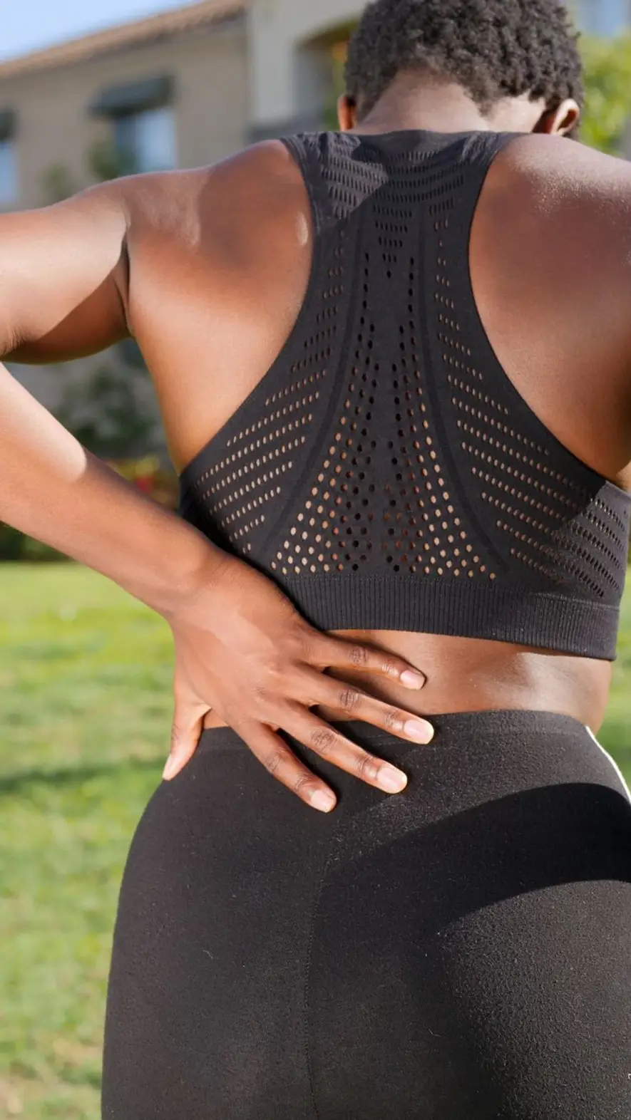 Pessoa em roupa de ginástica com as duas mãos apoiadas na parte baixa das costas, ao ar livre