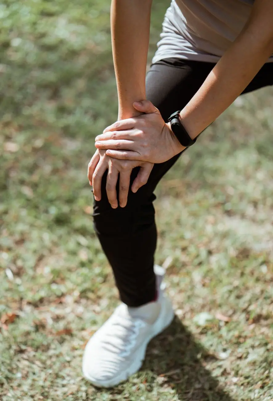 Pessoa em roupa de corrida com as duas mãos apoiadas sobre o joelho, em um gramado